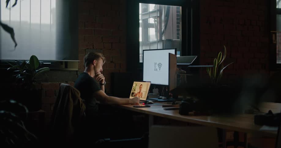 A man sitting on a chair at a desk with a laptop and computer