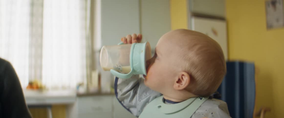 A young baby daughter smiles as she drinks from a cup while drinking while seated in a highchair