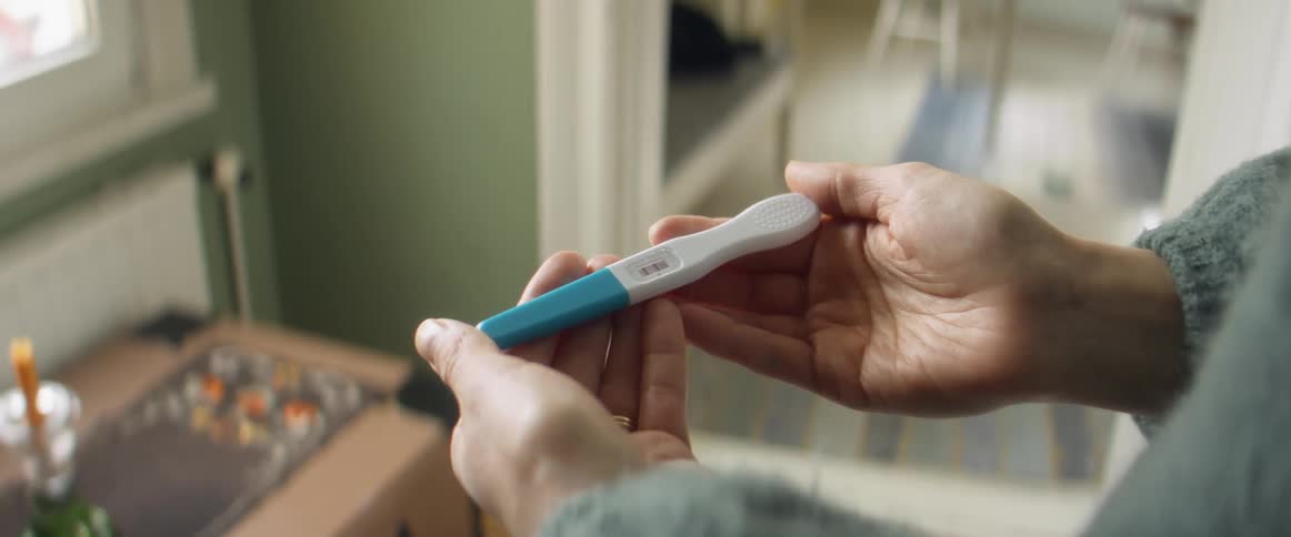 Person wearing sweater holds pregnancy test stick