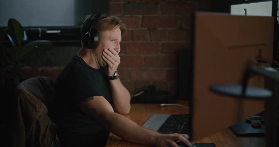 Man wearing headphones working on computer yawns