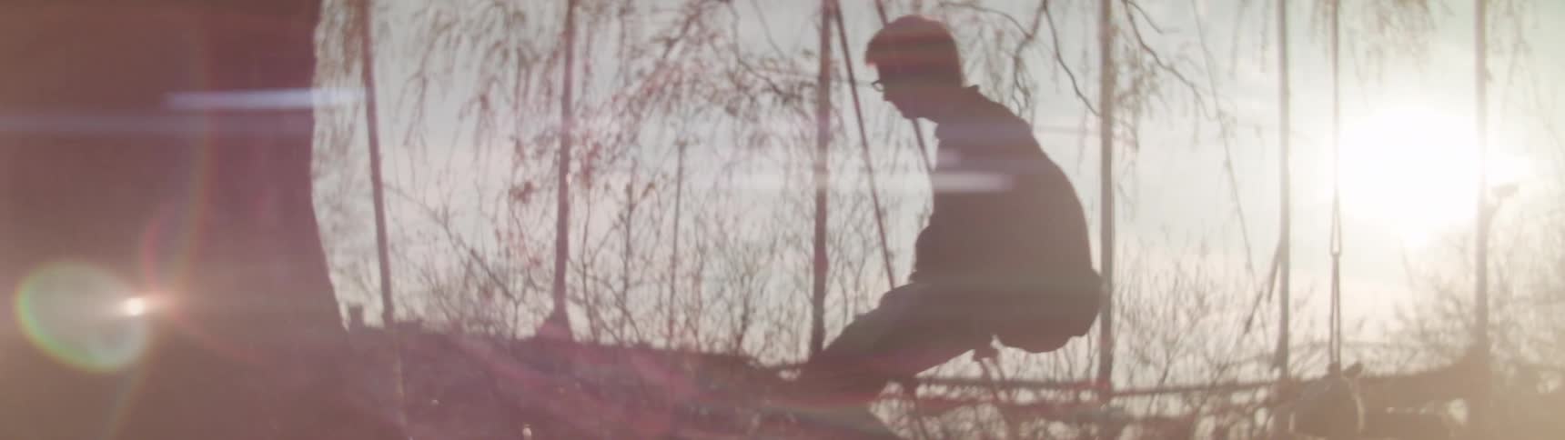 A man swings on a tree swing as the sun glares through bare trees