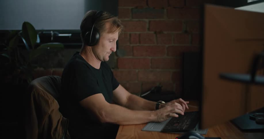 A man yawns takes off his headphones and gets back to work
