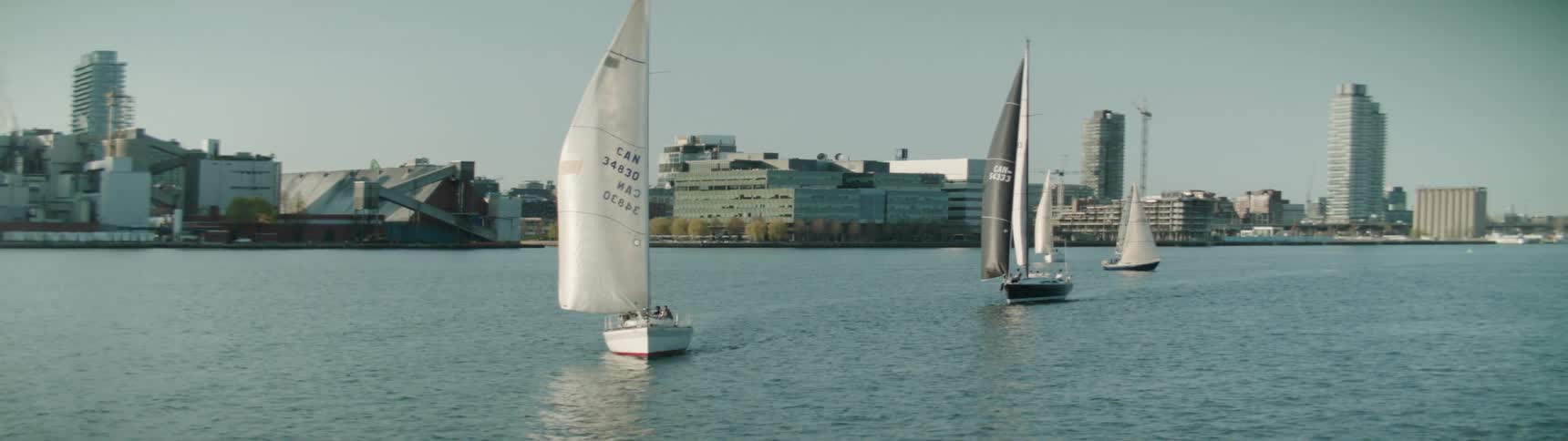 A coastal city with sailboats with buildings the sky and clouds in the background