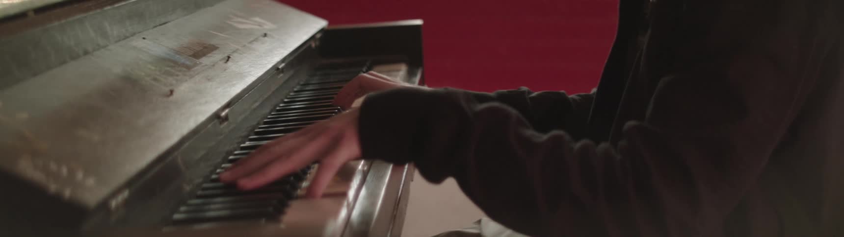 Person wearing long sleeve shirt plays piano in room with reddish walls
