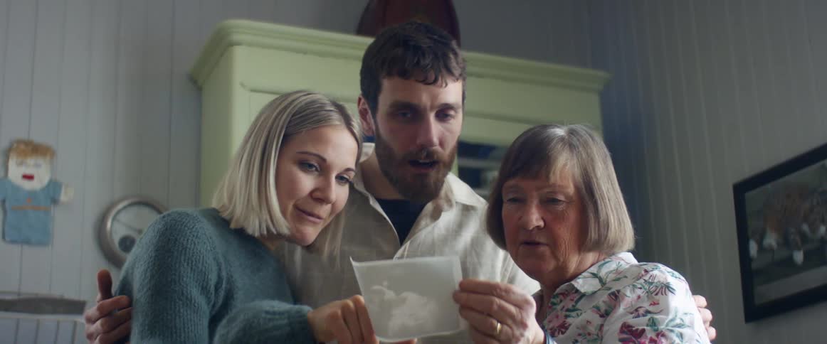 A couple show their mom an ultrasound photo as they stand in a nursery