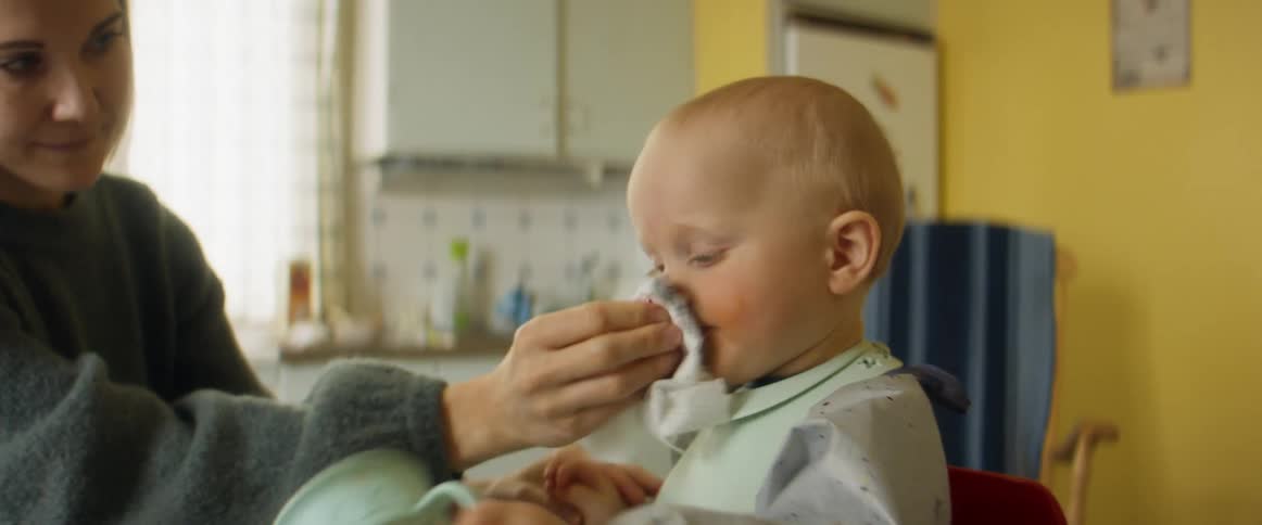 A baby turns a cup upside down while mom wipes his face