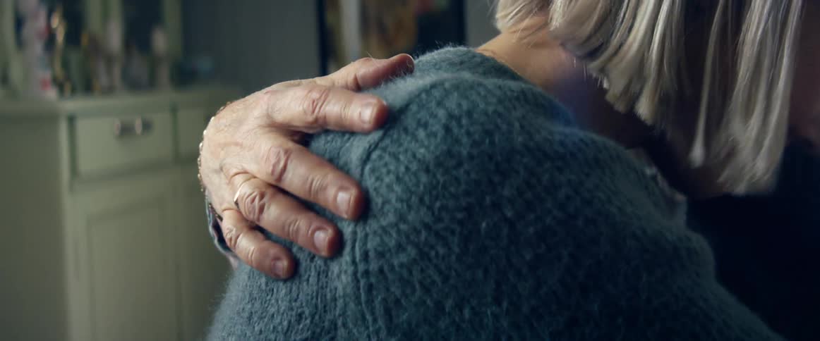 A wrinkled hand hugs and pats a womans back as an elderly mom comforts her daughter