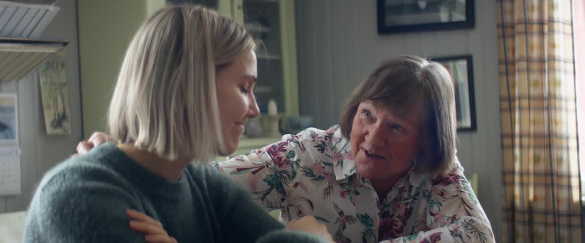 A woman comforts her daughter as they sit side by side at a table