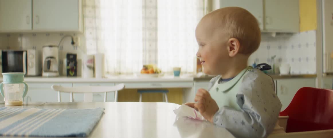 Toddler sitting at high chair smiles while wiping table