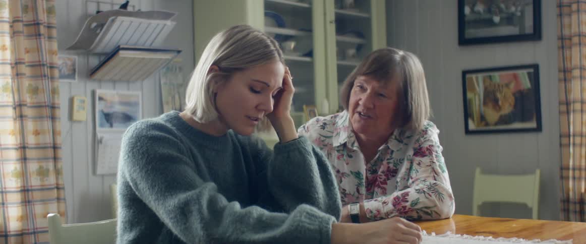 A crying young woman sits at a table while an older woman attempts to comfort her