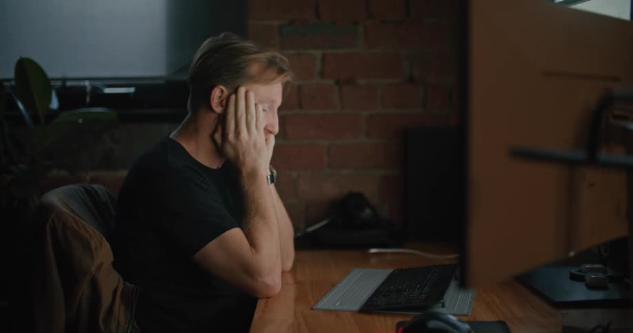 Man sits at desk rubbing his face before typing on keyboard