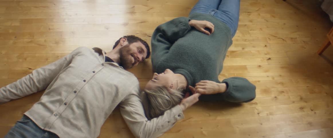A man and woman lying on the floor teasing smiling and holding hands