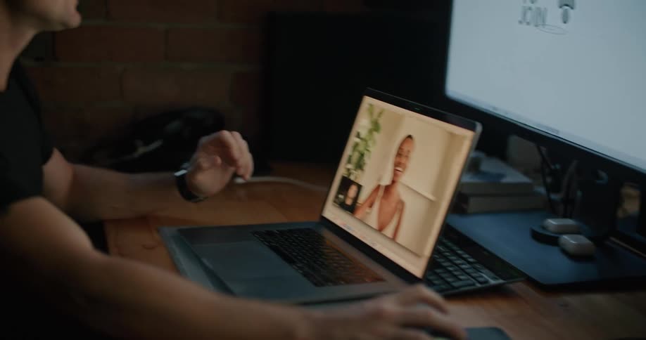 A man sitting at his desk at his office speaks with a colleague via video call on a laptop