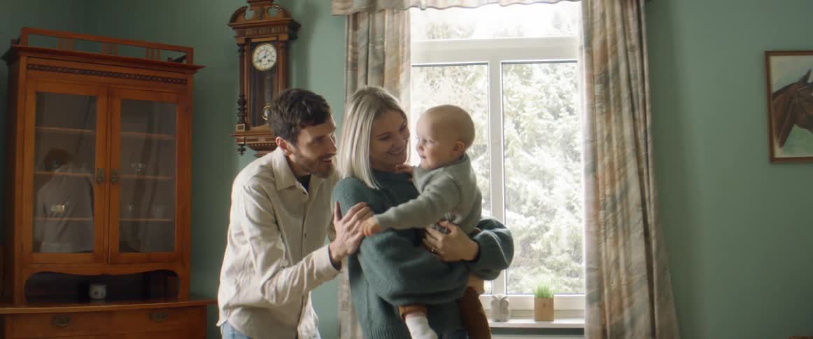 A dad plays peek a boo with his baby son held by mom