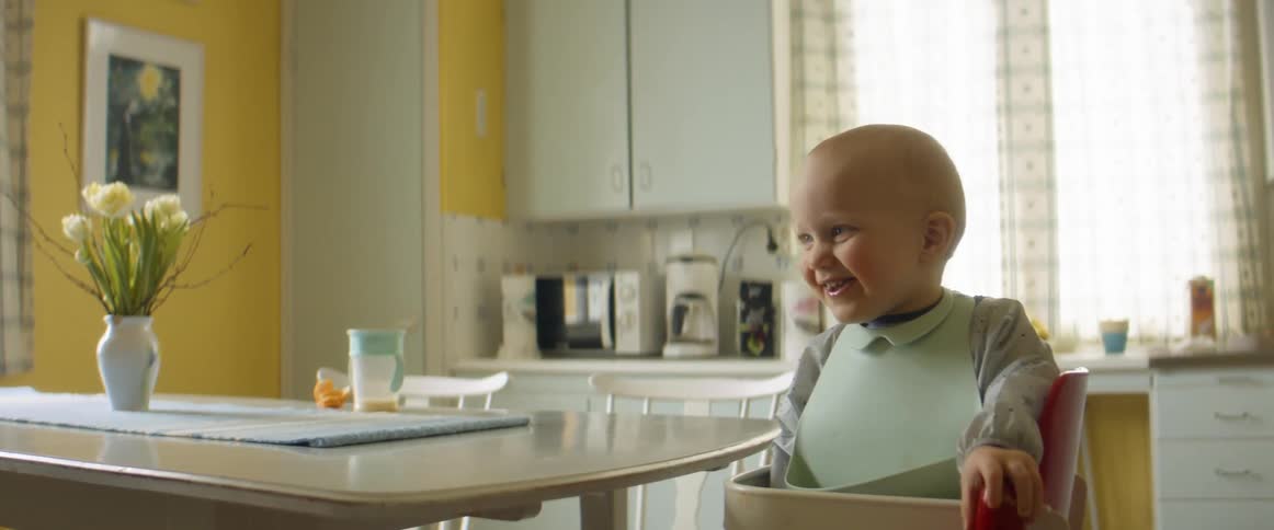 A young baby smiles and laughs while sitting in a highchair at a kitchen table