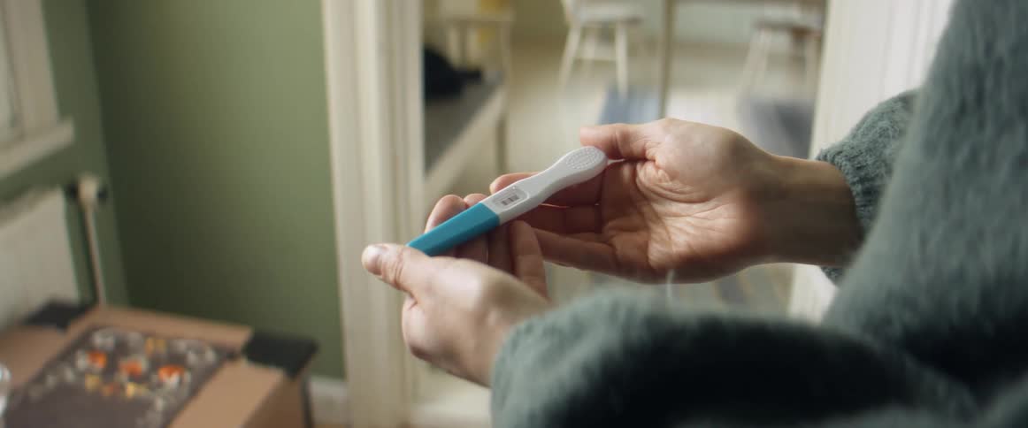 Woman with a pregnancy test in her hands standing in a room at home