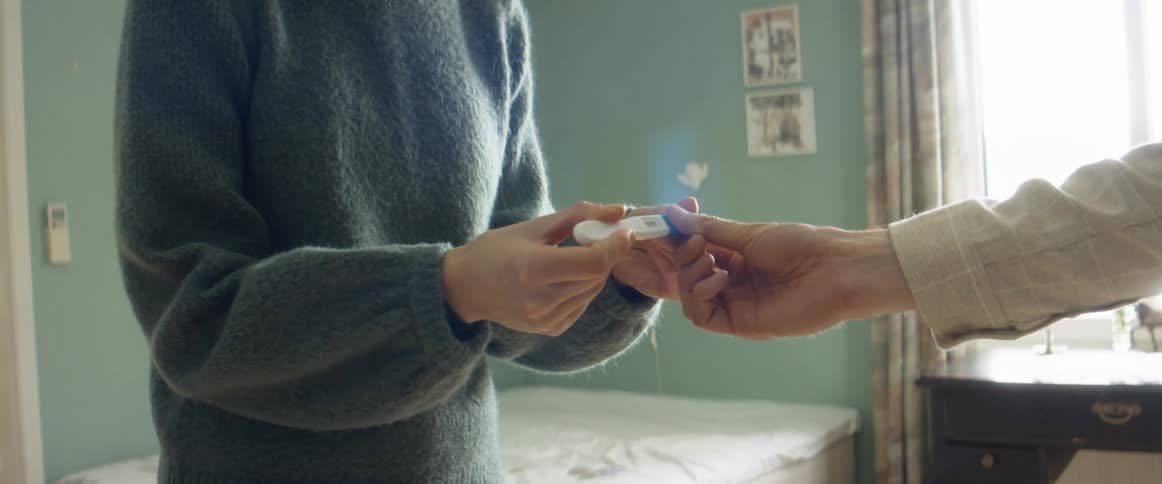 A woman runs into her bedroom and surprises her husband with a pregnancy test