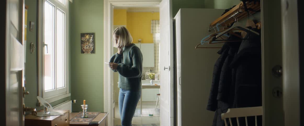 A woman standing indoors looks down ata pregnancy test and expresses happiness at the results