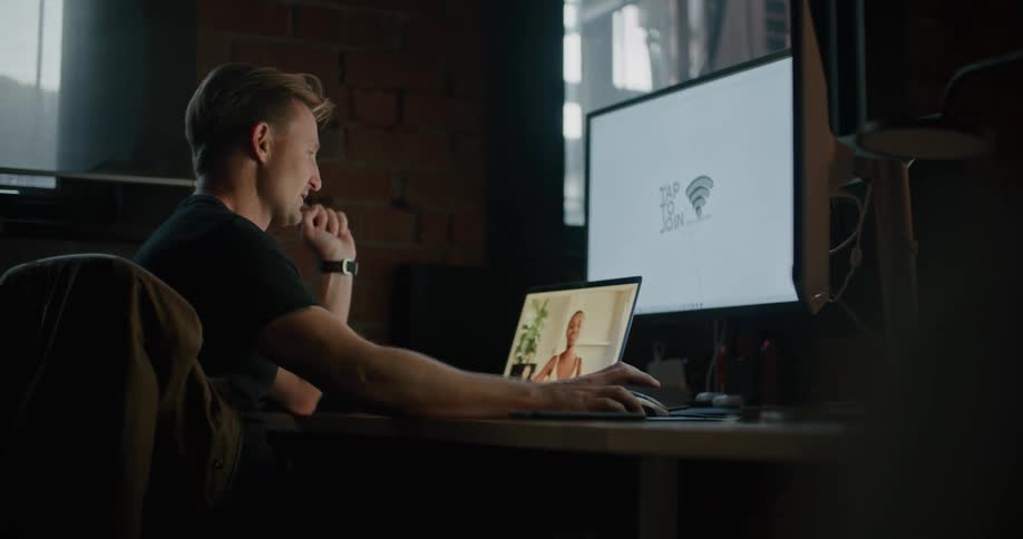 A man sitting on a chair at a desk with a laptop and computer