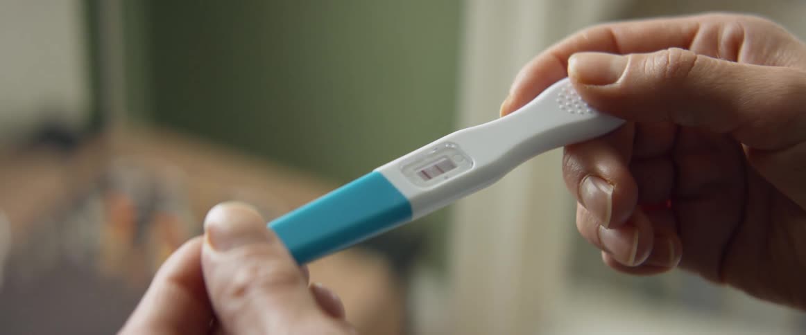 A woman holds a pregnancy test in her hands while reading the result