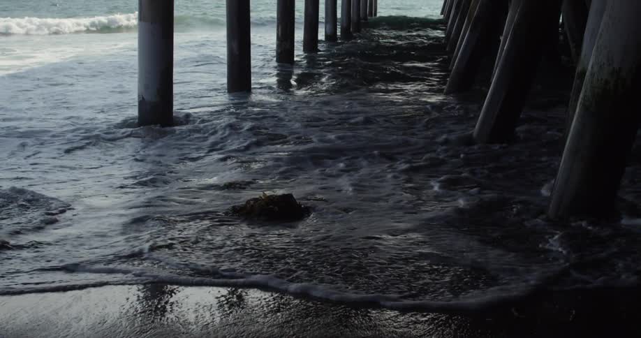 Waves crash against a pier on a beach