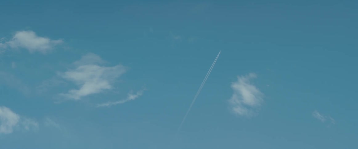 An airplane flying in the air with contrails with the sky and clouds above