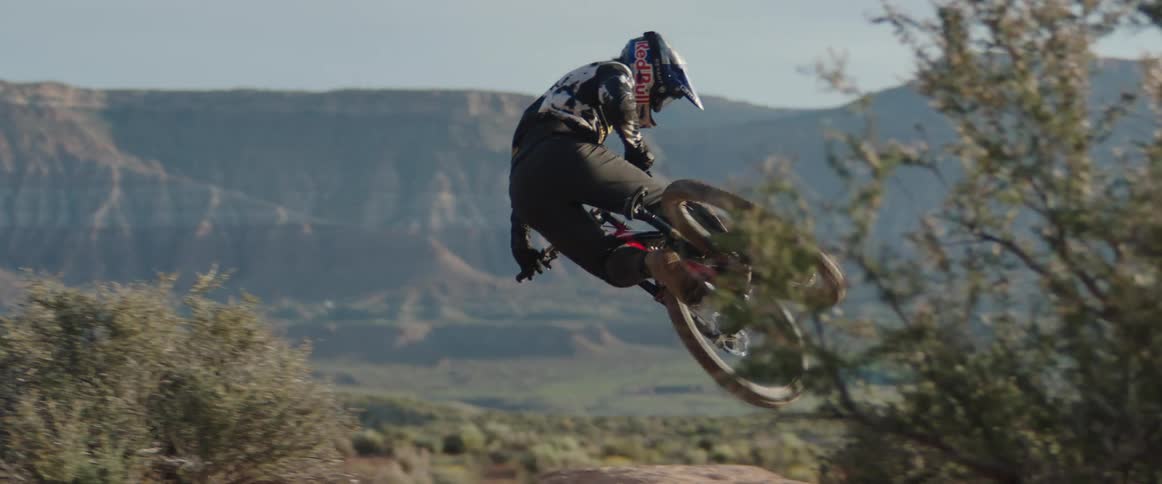 A person on a mountain bike whipping a jump in front of desert plateaus