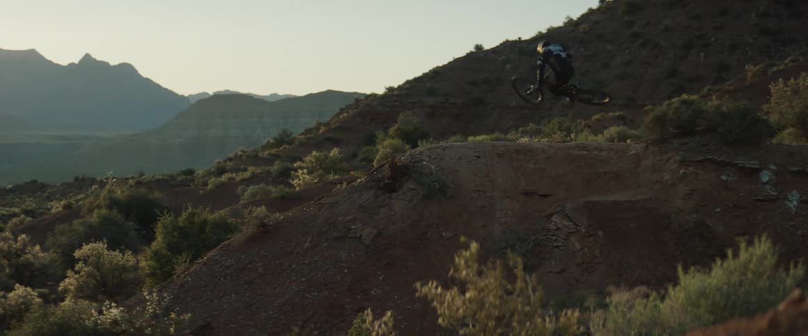 A mountain biker hits a jump in the desert with canyons and mesas visible