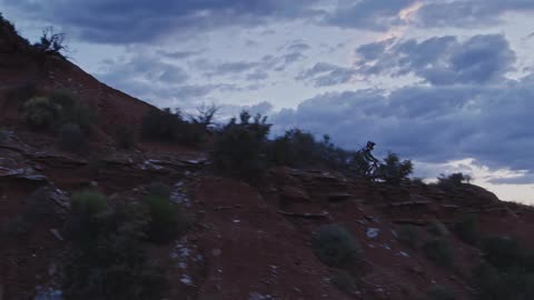 Man riding a mountain bike down the slope of a mountain in the desert at dusk