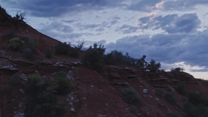 Man riding a mountain bike down the slope of a mountain in the desert at dusk