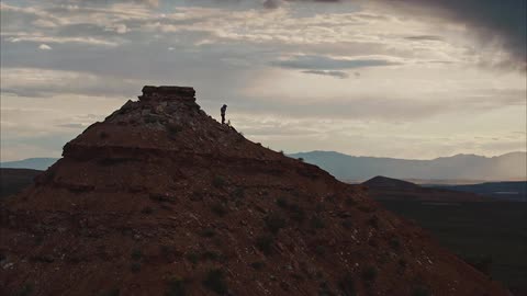 A mountain biker prepares to drop into a run from the top of a mountain under stormy desert skies
