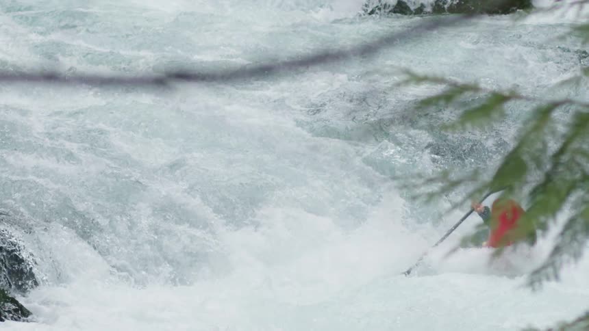 slowmotion shot of a man in a red whitewater kayak paddling through challenging whitewater in a clean and turbulent river canyon
