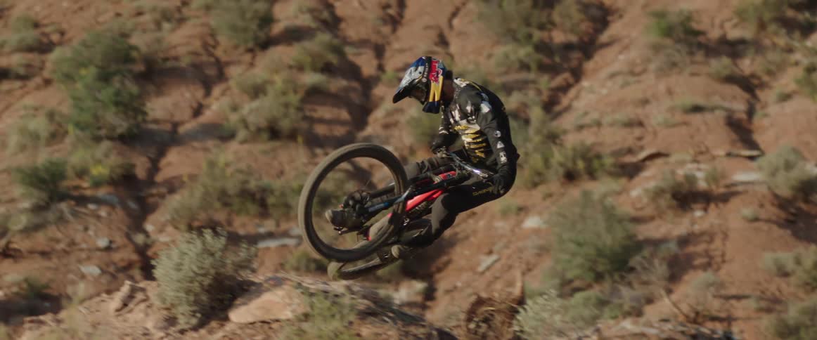 A person jumping and whipping a mountain bike over the crest of a desert landscape