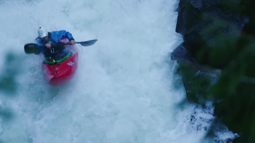 Slow motion shot of a man in a red whitewater kayak riding over a double drop waterfall in the Pacific Northwest in early Spring