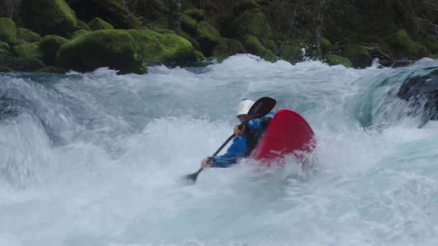 Real time clip of a man in a red whitewater kayak shredding a steep and turbulent whitewater rapid on a clean clear river