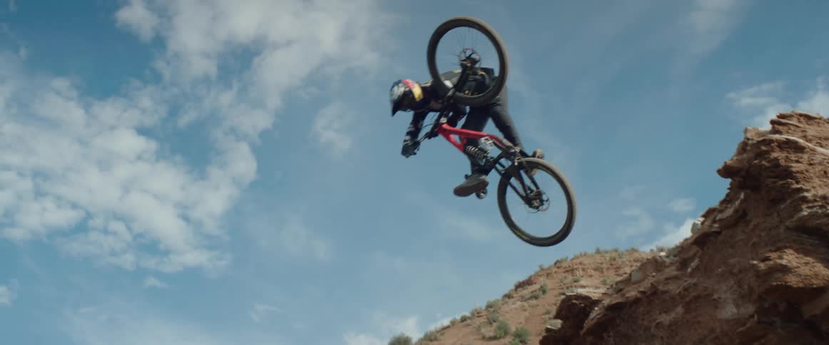 A man jumping a mountain bike off a cliff and performing a shoulder buzz trick