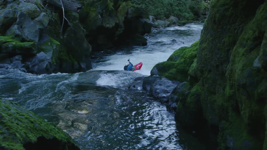 Real time shot of a man in a red whitewater kayak paddling in a narrow and green river valley down awesome whitewater