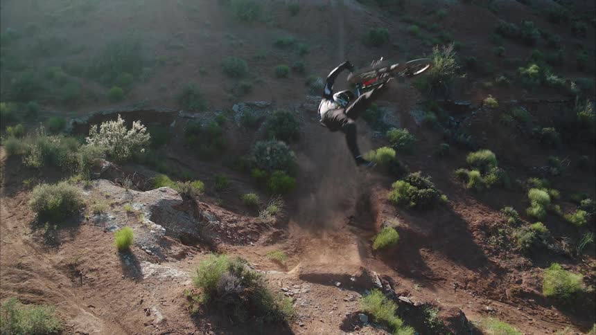 A mountain biker flips their bike on a desert jump underneath the camera