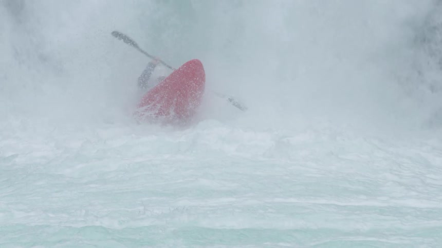 Slow motion shot of a whitewater kayak paddling over a steep waterfall before emerging below and sprinting straight towards camera