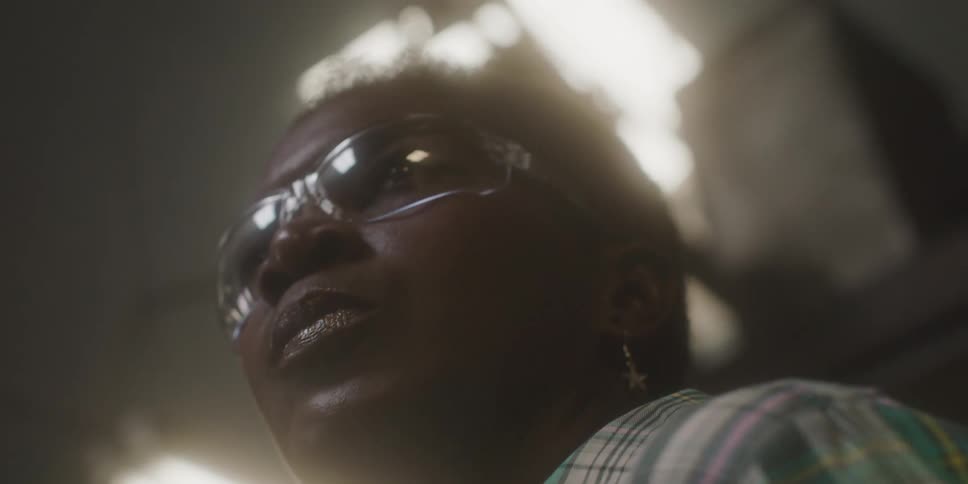 A woman with goggles in a workshop with shelves and lights in the background