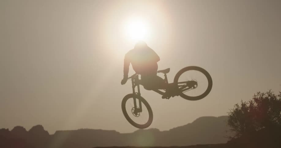 A mountain biker whips their bike sideways off a jump through the rising sun