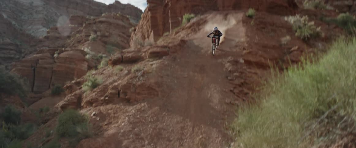 A mountain biker hits a cliff drop and then rides into a dirt corner