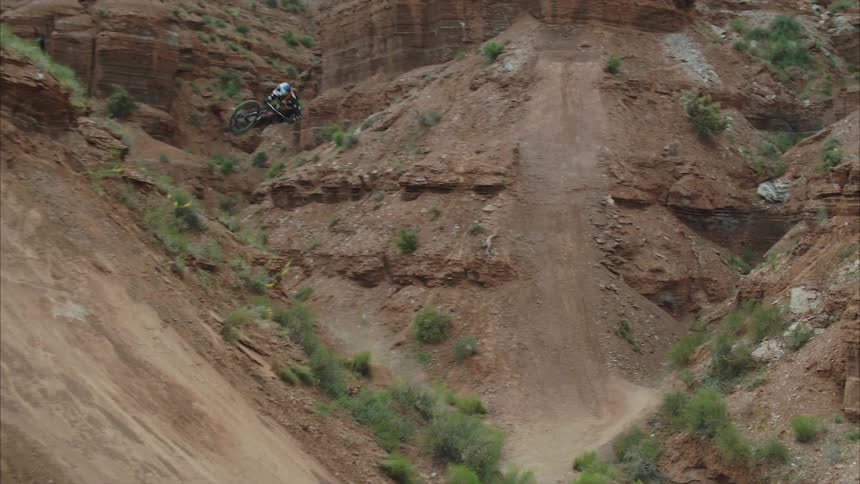 A man riding a mountain bike down a hill and hitting a hip jump in the desert