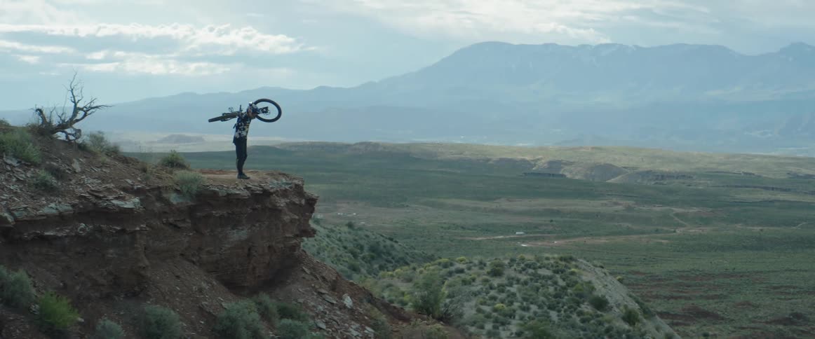 Bicyclist carries his bike to the edge of a desert cliff to examine drop