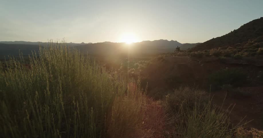 Bicyclists hits a jump as the sun rises over the desert landscape