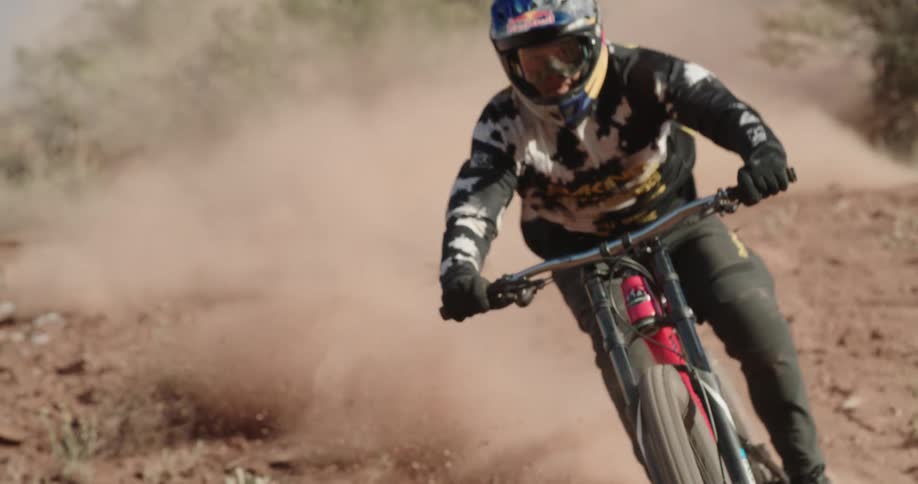 A mountain bike athlete carves down a steep dirt chute kicking up clouds of dust