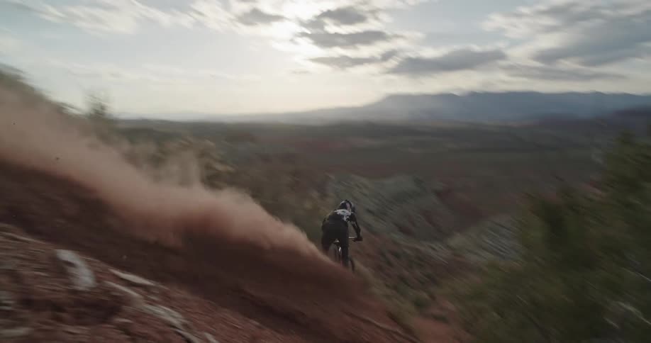 A mountain biker races down a steep desert chute in front of the valley sunset