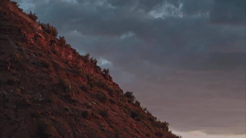 Mountain biker descends steep desert chute against stormy sunset