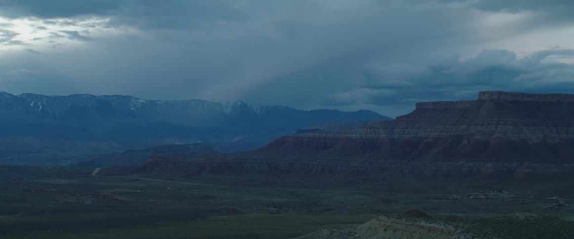 Mesas with a valley below and mountains in the distance under a cloudy sky