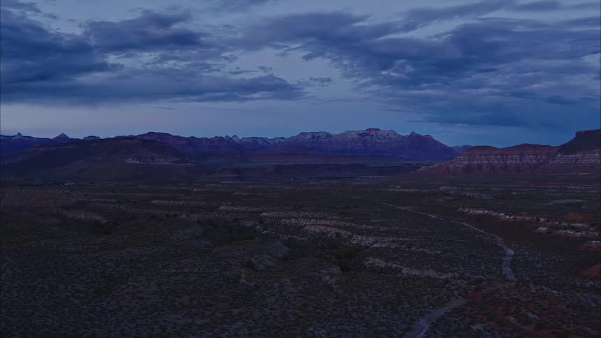 Sweeping aerial of desert landscape with distant plateaus and barren road at dusk